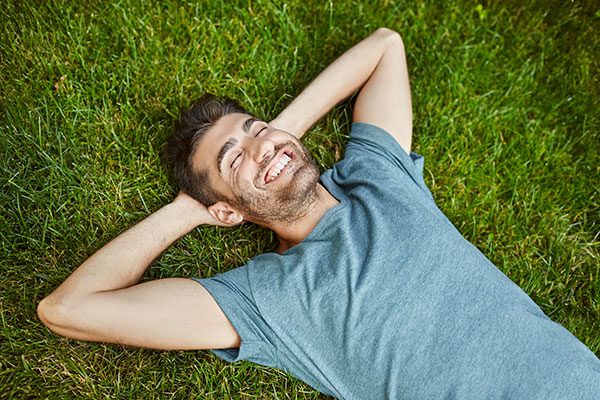 positive-emotions-young-beautiful-bearded-caucasian-male-in-blue-t-shirt-lying-on-grass-smiling-with-teeth-laughing-relaxing-outside-in-summer-morning-with-happy-face-expression
